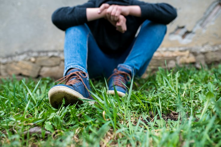 Frustrated teenage boy sitting near a crumbling wall at the correctional institute