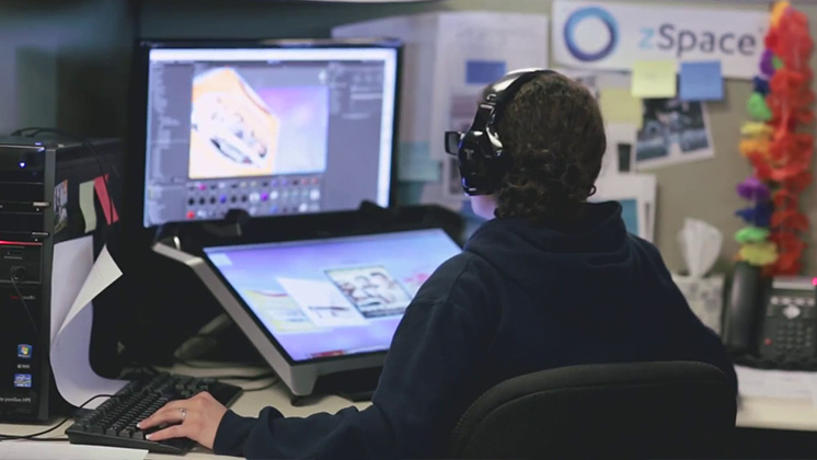 Person wearing headphones working on a 3D modeling project using zSpace technology. Seated at a desk with dual monitors, one displaying a 3D model and the other a digital workspace, the individual is immersed in their task.