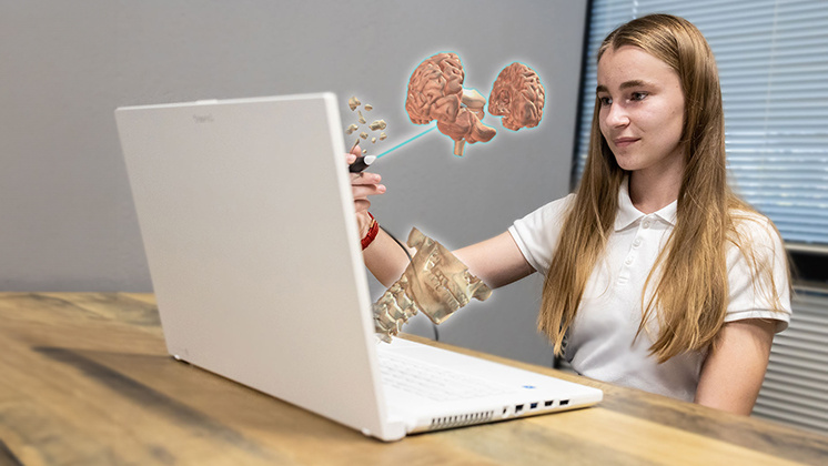 A student using a zSpace laptop with augmented reality (AR) technology to study human anatomy. The student is holding a stylus and interacting with a 3D model of a human brain that appears to float above the laptop screen.