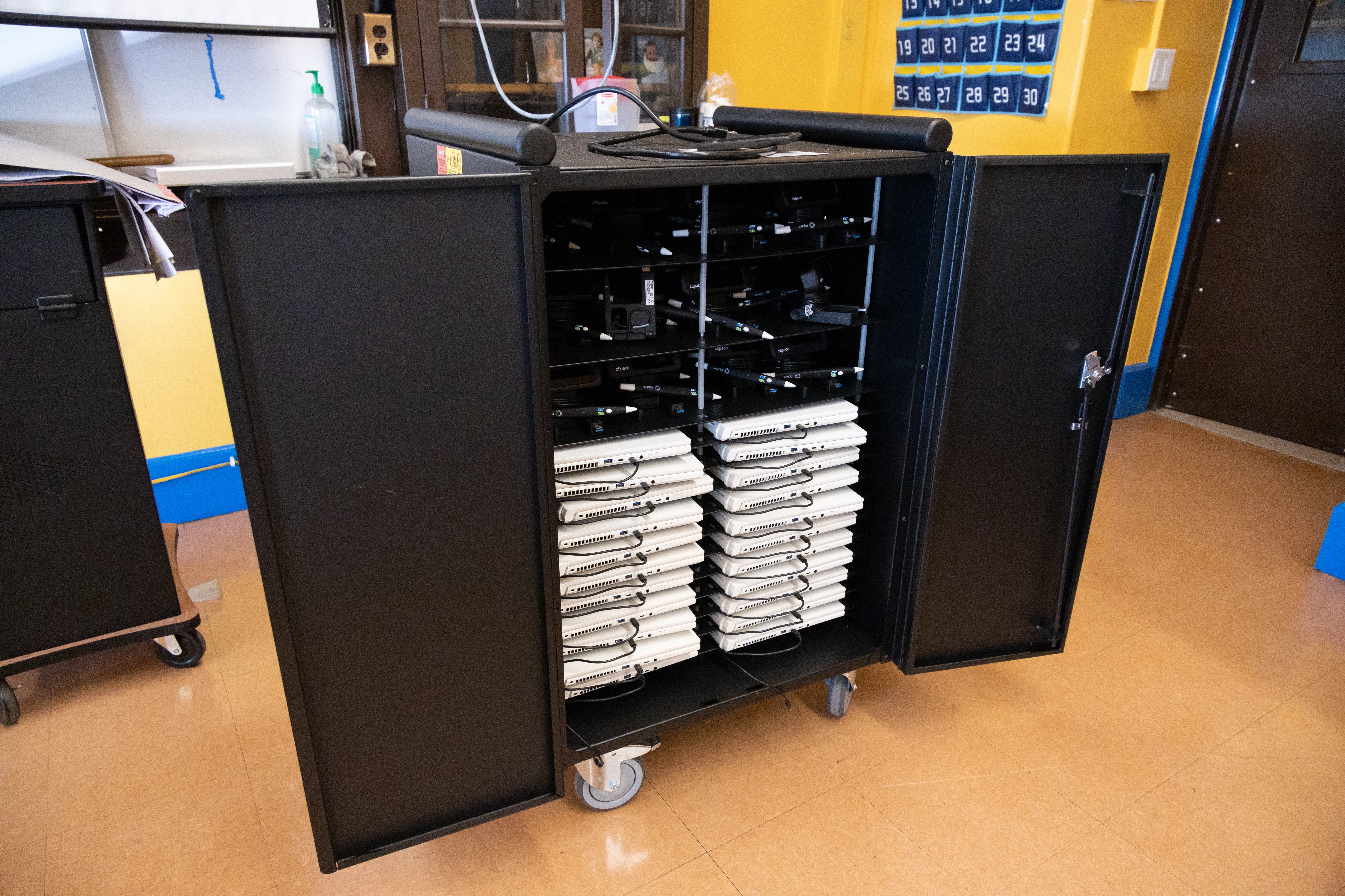 Mobile charging cart filled with laptops in an organized classroom setting, highlighting efficient storage and charging solutions for educational technology integration.