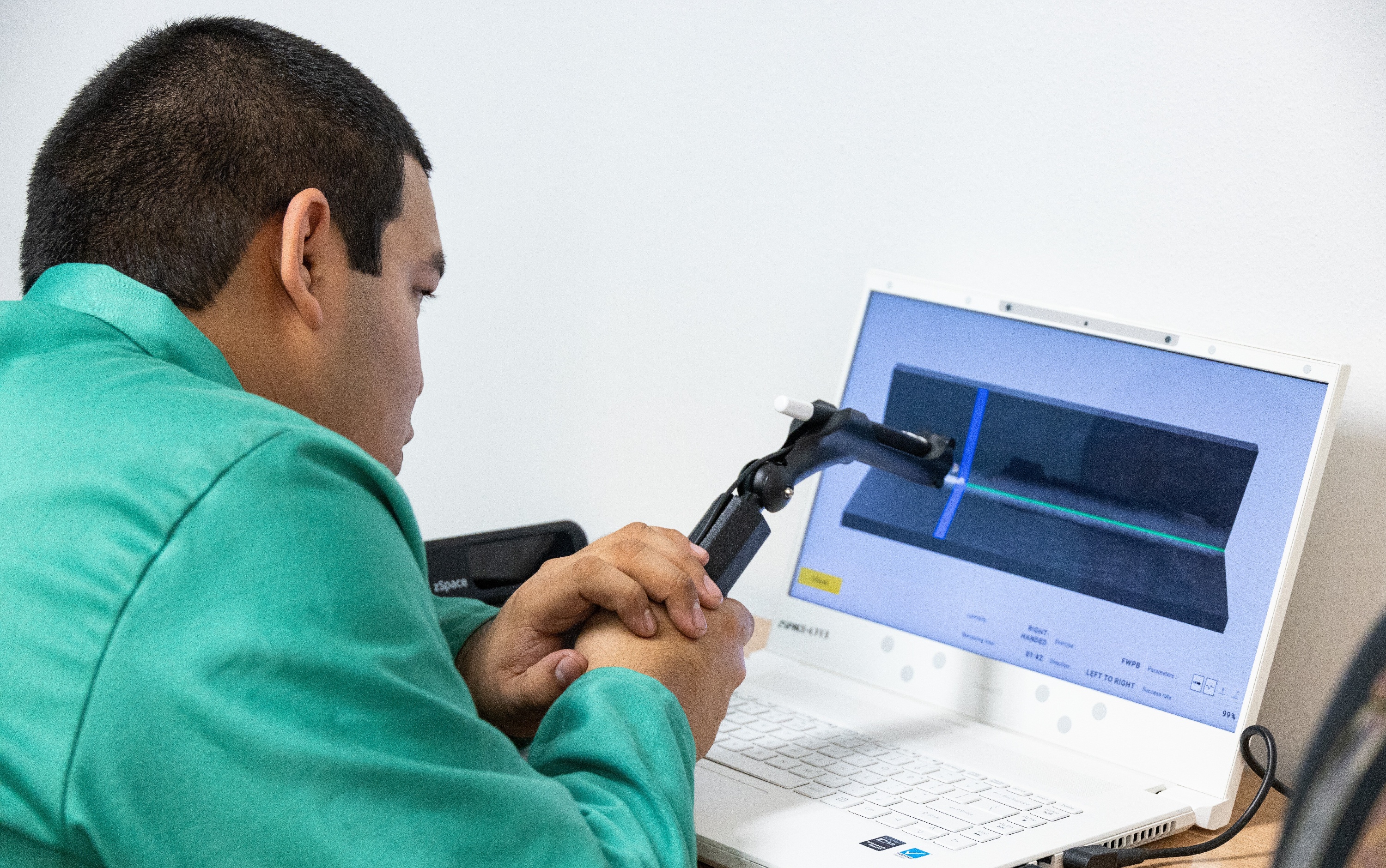 High school student in green shirt using a welding torch connected to a laptop displaying a 3D model simulation, emphasizing precise control and tactile feedback in virtual applications.