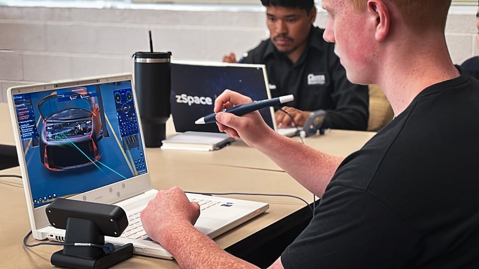 A high school student uses a stylus to interact with a 3D car model on a zSpace laptop during a classroom session.