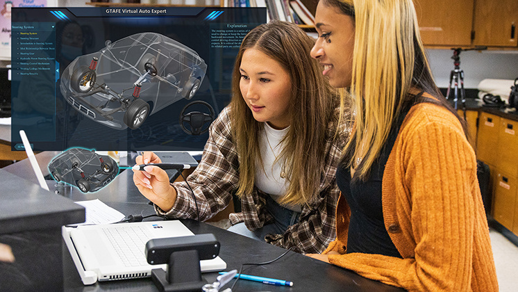 Two students using zSpace's GTAFE Virtual Auto Expert software in a classroom to study a 3D model of a car's internal components. They are examining detailed views of the suspension and steering systems with a stylus.
