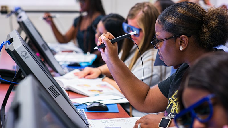 Students using zSpace technology in a classroom setting, engaging with interactive digital content on touchscreen monitors with stylus pens.