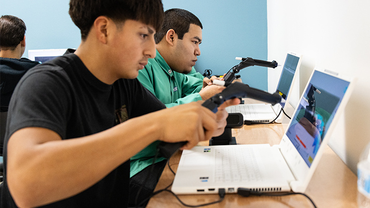 Students using zSpace laptops with virtual reality welding torch controllers to engage in interactive learning activities. This image highlights the use of advanced technology in education, providing immersive and hands-on learning experiences with zSpace.