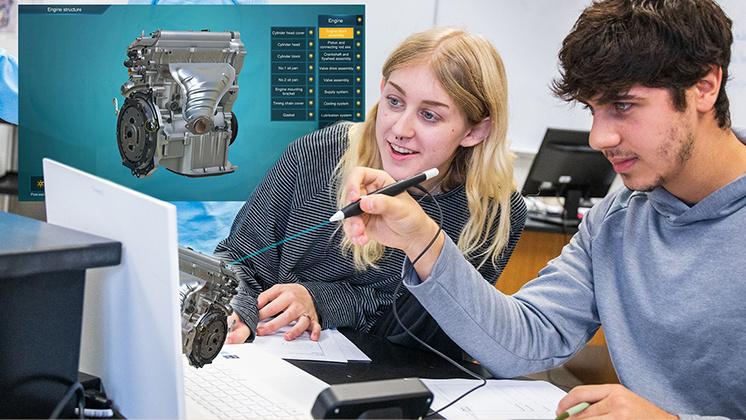 Two students using a zSpace augmented reality system to study an engine structure. They are interacting with a 3D model of an engine displayed on a computer screen, using a stylus to manipulate the model. The background shows a detailed engine diagram with labeled parts.