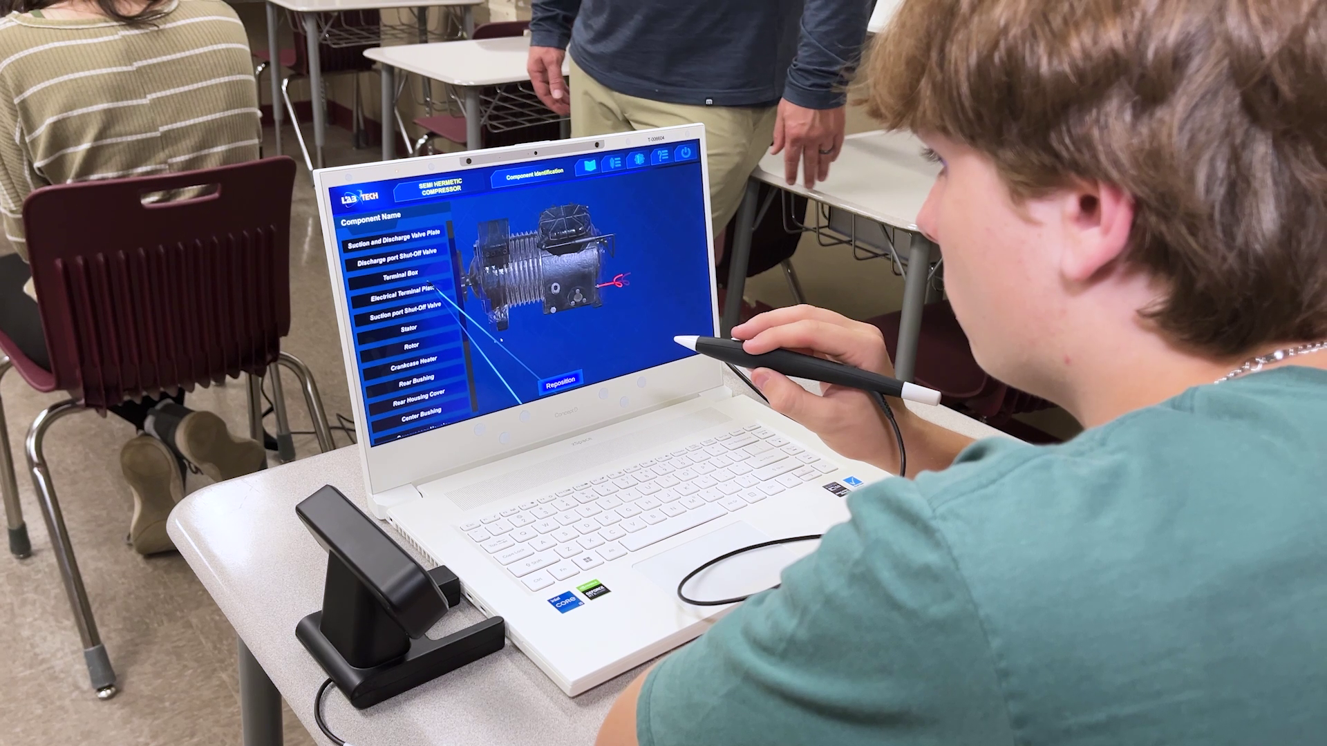 High school boy using a white laptop on classroom desk, focused on the screen with an expression of curiosity and concentration.