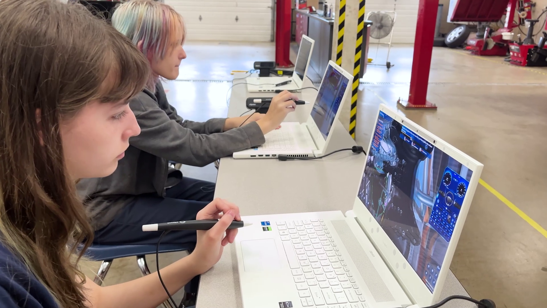 Two high school automotive students engage with interactive AR/VR content on zSpace laptops using a stylus in a classroom setting.