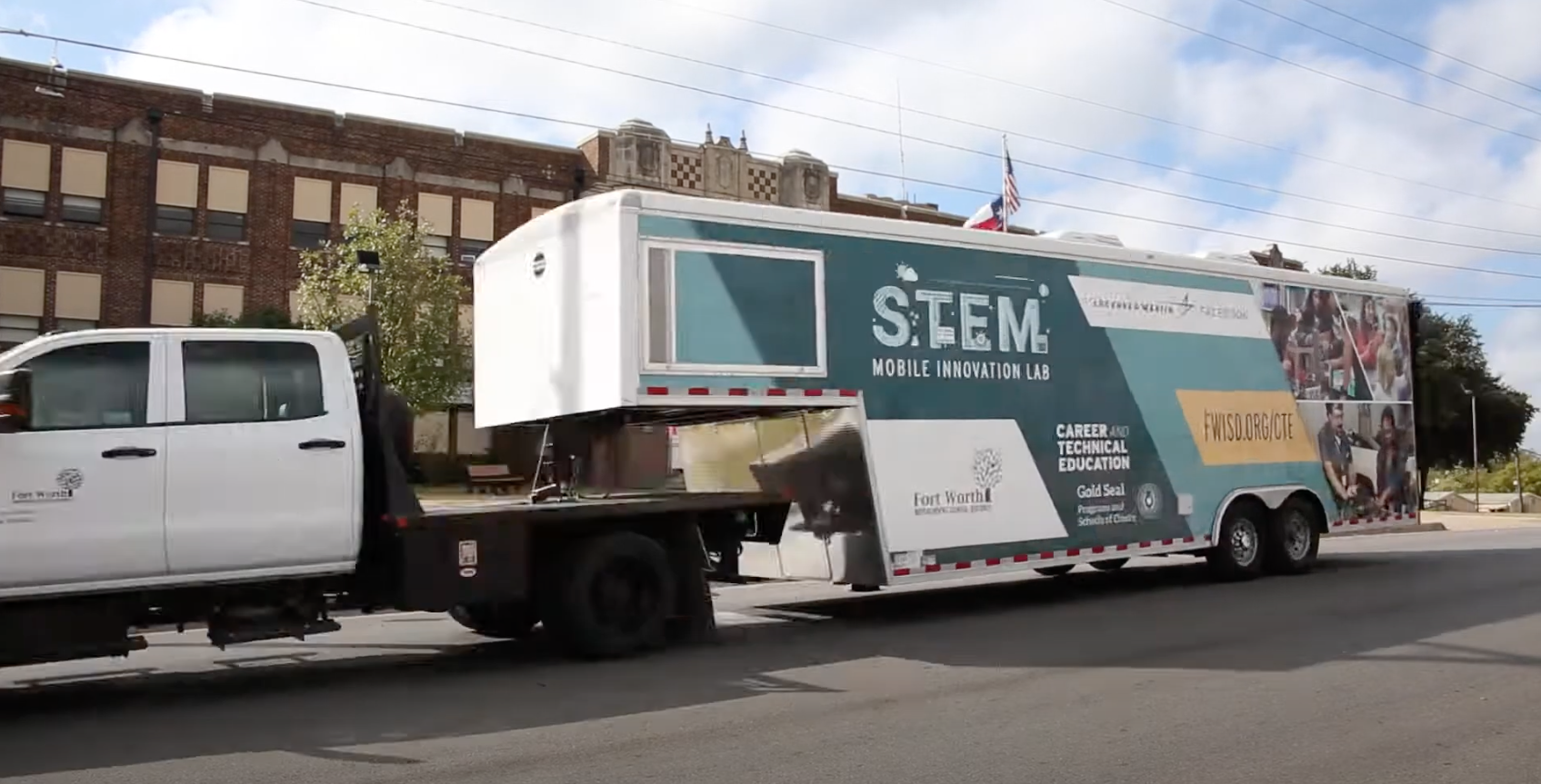 White truck towing a large trailer labeled 'STEM Mobile Innovation Lab' in front of a brick building. The trailer features graphics and text promoting career and technical education, including the Fort Worth Independent School District (FWISD) and a website link fwisd.org/cte.